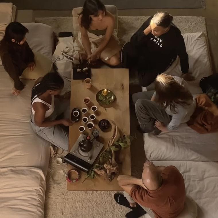 People sitting on floor cushions around a low wooden table set with small tea cups