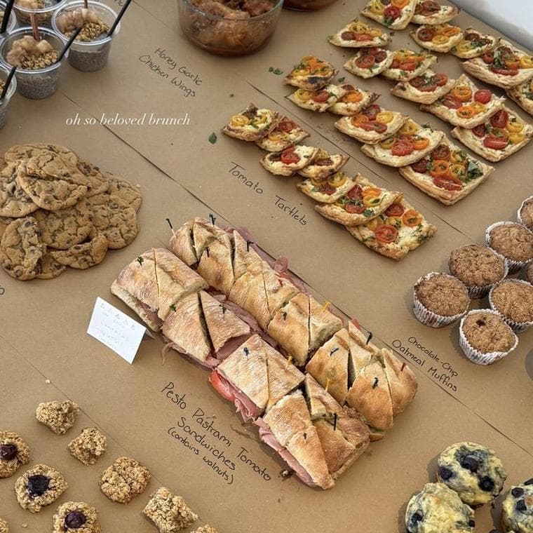 A long table of food laid out on brown paper with each dish labelled in marker