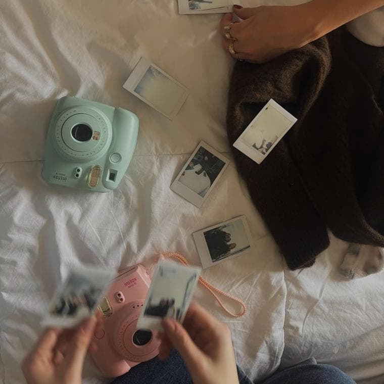Two instant cameras and a scatter of small printed photos on a white bed
